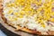 Closeup of a whole delicious pizza with melted cheese, corn and onions on a board
