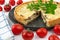 Closeup wide studio shot of freshly baked yellow French salty cake, or quiche with mushrooms, red cherry tomatoes, green mint and