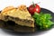 Closeup wide studio shot of a slice of yellow French salty cake, or quiche, with mushrooms on a black design plate, isolated on