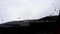 Closeup window with rain drops, blurred cloudy sky and roof of the house in background.