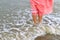Closeup of a woman bare feet standing at sandy beach, with a wave foaming - travel and relaxing. Female leg walking on the beach.