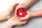 Closeup of woman and child holding heart on grey stone background, top view. Donation