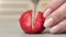 Closeup woman fingers cutting whole fresh red strawberry to half on wooden kitchen table use knife