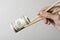 Closeup of woman hand holding chopsticks and money against white wall