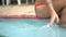 Closeup of woman hand playing in water while sitting on edge of outdoor swimming pool