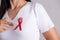 Closeup of woman hand pointing to red badge ribbon on chest to support AIDS Day. Healthcare, medicine and AIDS awareness concept