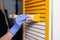 Closeup woman hand in purple rubber glove with paint brush painting natural wooden door with yellow paint, creative design house
