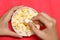 Closeup woman hand taking popcorn from white bowl on red  table background