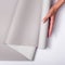 Closeup of a woman holding a roll of gray wallpaper against a white background