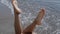 Closeup woman legs waving in front ocean waves sunny day. Girl lying wet beach.