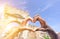 Closeup of woman and man hands showing heart shape during romantic vacation - Young multiracial couple making love symbol next a