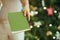 Closeup on woman near Christmas tree giving green notebook