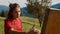 Closeup woman painter drawing picture in mountains. Girl painting on easel.