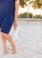 Closeup of woman\'s legs on the sandy ocean beach. Girl standing on the sand and holding white sneakers boots. outdoors