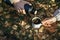 Closeup of woman`s and man`s hands holding metal cup and thermos bottle and pouring tea in the woods outdoors