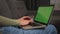 Closeup. Woman using laptop with green screen, typing on keyboard, sitting on the couch sofa at the home. Chromakey.