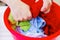 Closeup womans hands handwashing clothes in red plastic washbucket, scrubbing and squeezing fabrics, laundry housework concept