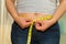 Closeup womans stomach with shirt lifted up, wearing jeans, measuring waistline using measure band, weightloss concept