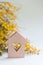 Closeup wooden house with hole in form of heart with yellow mimosa branches on lilac background with copy space