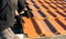Closeup of worker hands installing yellow ceramic roofing tiles mounted on wooden boards covering residential building roof under