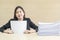 Closeup working woman are boring from pile of work paper in front of her in work concept on blurred wooden desk and wooden wall