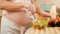 Closeup of yougn pregnant woman with big belly eating fresh vegetable salad while standing on kitchen. Concept of