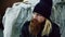 Closeup of young bearded homeless man sitting near shopping cart upet and stressed alone in the street