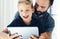 Closeup of young boy sitting with father at the table and using pc tablet in modern loft. Horizontal, blurred background.