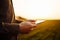 Closeup of young farmer`s hands holding a tablet and checking the progress of the harvest at the green wheat field on the sunset.