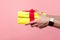 Closeup of young male hands giving yellow gift box with red ribbon. isolated on pink background