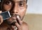 A closeup of a young man trimming his beard with an electric trimmer