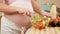 Closeup of young pregnant woman with big belly eating fresh vegetable salad while standing on kitchen. Concept of