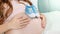Closeup of young pregnant woman lying in bed and holding blue newborn baby boots on big belly. Concept of pregnancy