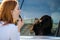 Closeup of a young redhead woman driver correcting her makeup with dark red lipstick looking in car reflective window