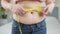 Closeup of young woman with fat belly measuring her waistline.