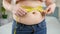 Closeup of young woman with fat belly measuring her waistline. Concept of dieting, unhealthy lifestyle, overweight and