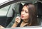 Closeup young woman sitting in car putting on makeup looking in mirror, as seen from outside drivers window, female