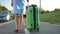 Closeup of young woman walking on city sidewalk with green suitcase on summer day.
