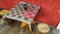 Cloth checker board. Outdoors with wood stools and red wall.