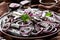Cloth-up of salted sprats marinated with red onion rings on an earthenware plate coriander seeds, brown cloth, fork and knife on