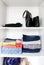 Clothes sorting in home wardrobe. Different clothing items and bag accessories on white shelf