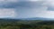 Cloudburst above hills overgrown in forests during summer