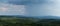 Cloudburst above hills overgrown in forests during summer