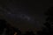 Cloudless starlit night sky with Milky Way and bright stars with firelight and trees in the background as panorama view