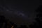 Cloudless starlit night sky with Milky Way and bright stars with firelight and trees in the background as panorama view