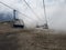 Clouds enveloping modern ropeway with benches in amazing mountainous terrain.