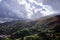 clouds loom over a landscape with green hills and trees