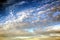 The clouds are multicolored, thunderous bizarre shapes against the blue sky and the sun above the ocean surface.