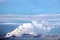 The clouds are multicolored, thunderous bizarre shapes against the blue sky and the sun above the ocean surface.