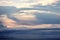 The clouds are multicolored, thunderous bizarre shapes against the blue sky and the sun above the ocean surface.